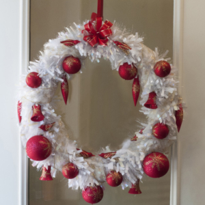 A white Christmas wreath with red ornaments