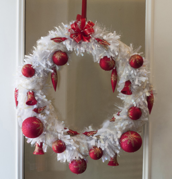 A white Christmas wreath with red ornaments